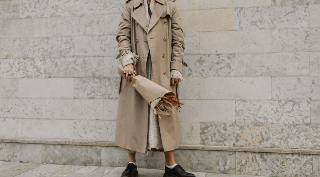 Person i beige trenchcoat med stickade lager och bukett