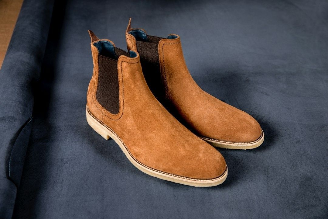 Ett par bruna mockaboots med resår och ljusa sulor på mörkt tyg
