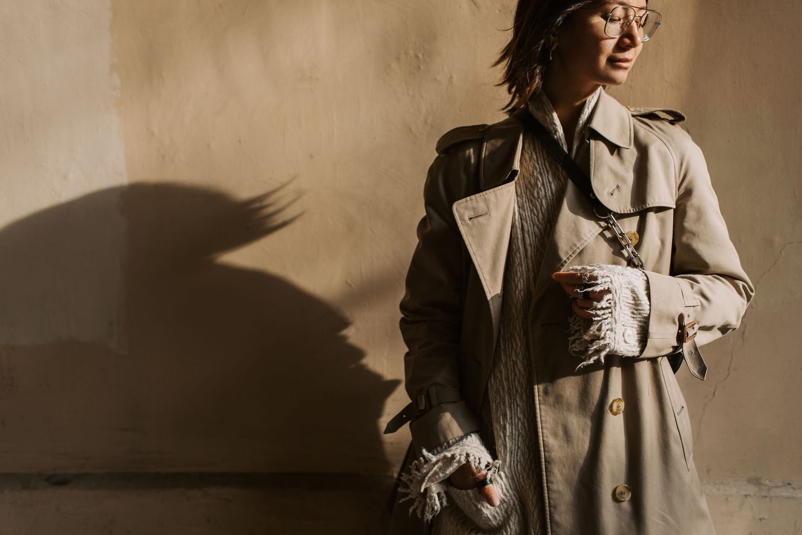 Person i trenchcoat med stickade lager och halsduk i varmt solljus