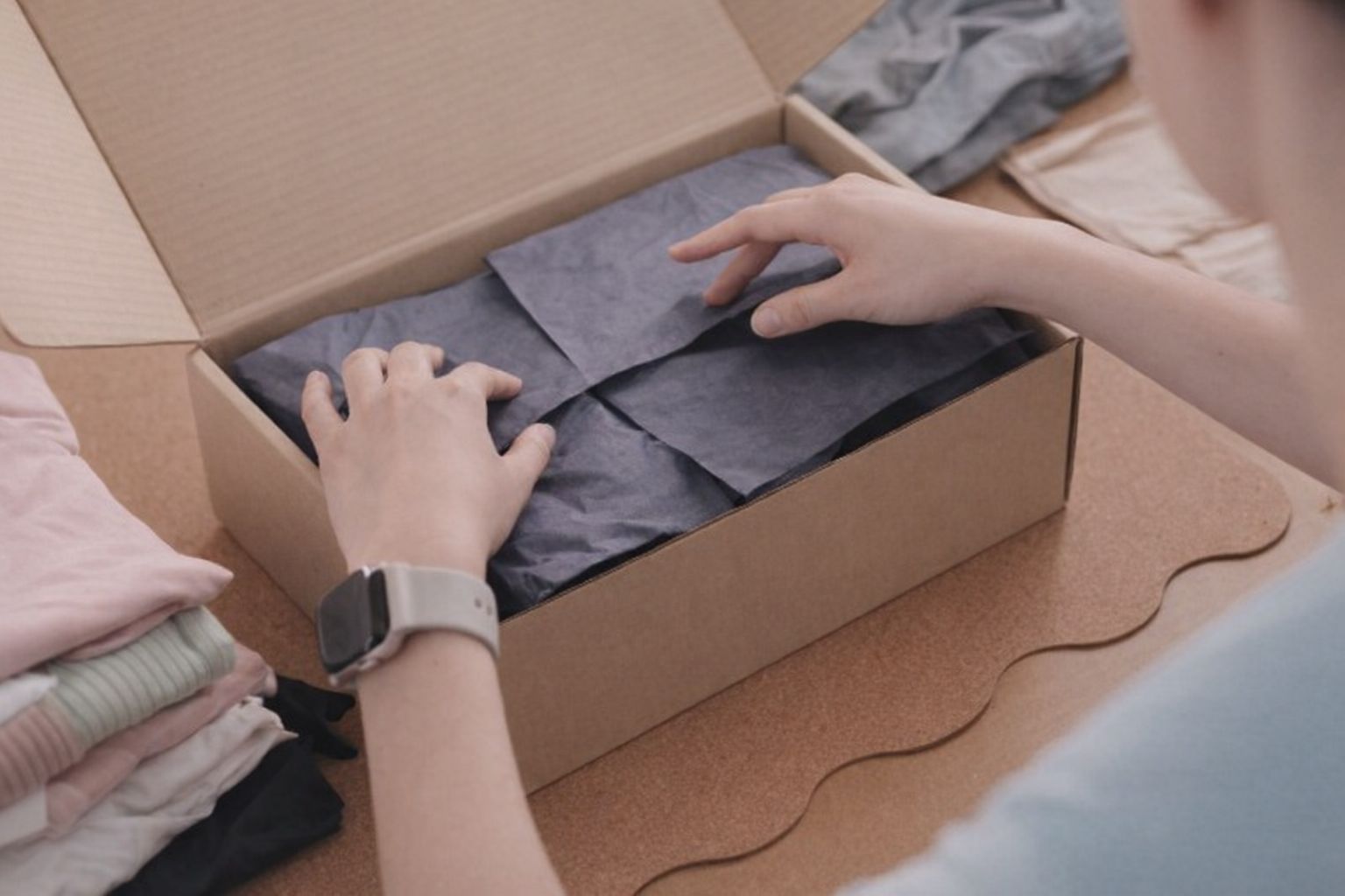 En person packar kläder i en kartong med silkespapper för frakt.